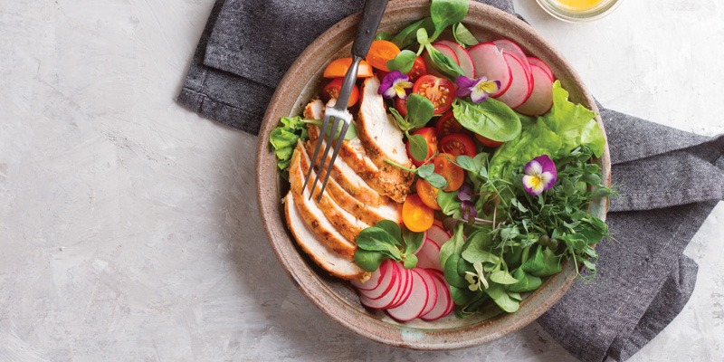 Salad with chicken, tomatoes, flowers, and radishes in a bowl