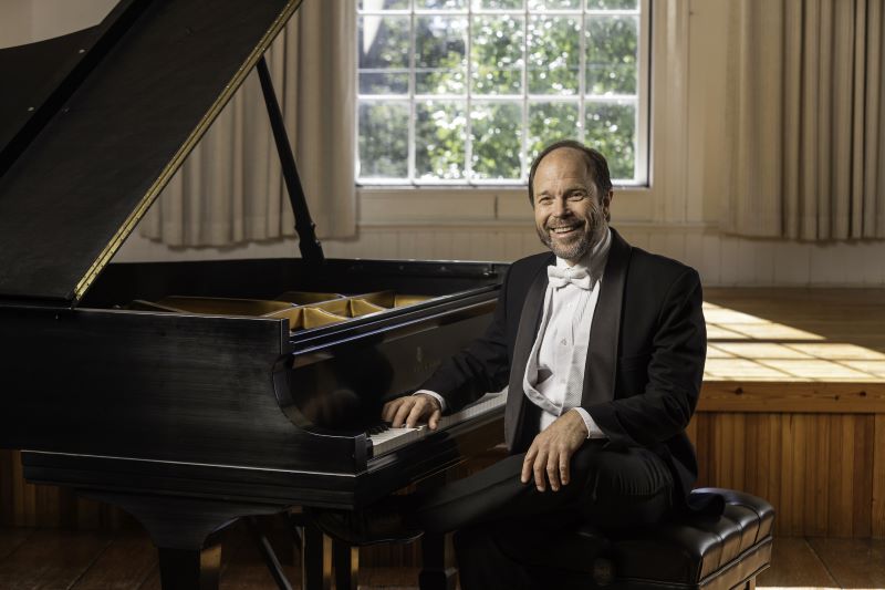 Fred Moyer sitting at the piano in a suit smiling at the camera